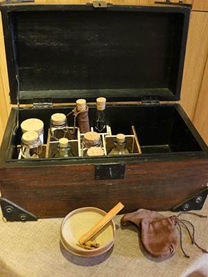 Coffre en bois ouvert présentant des épices dans des bocaux et files en verre